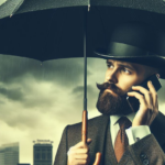 Man with bowler hat, 3 piece suit holds an umbrella overhead as he makes a call on a cellphone.